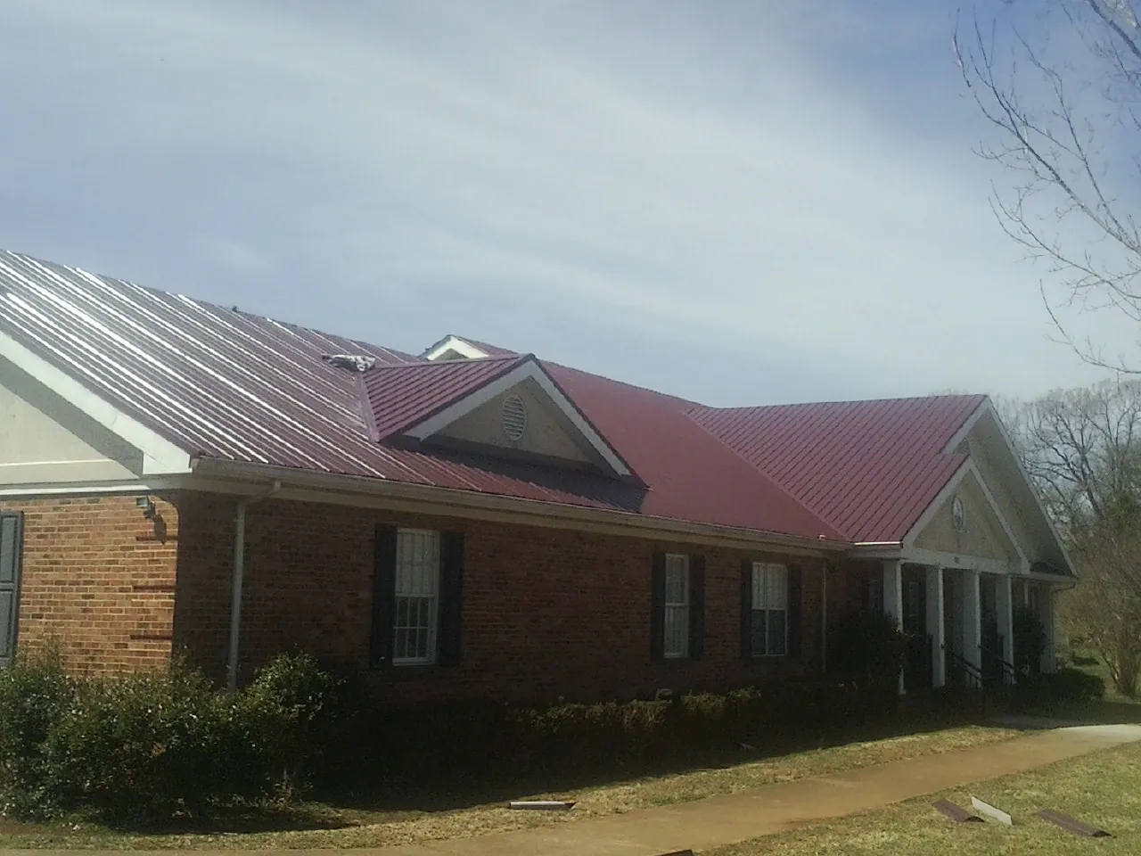 Red metal roof with gabled entries on a long brick building, from a Hail Damage Roof Repair job in Rock Island