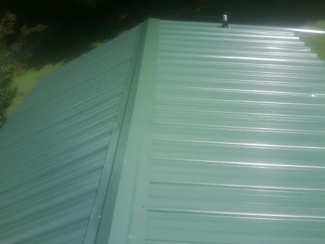 New green metal panels meeting at the ridge of a roof — Flat Roof Repair work by our crew in Rock Island