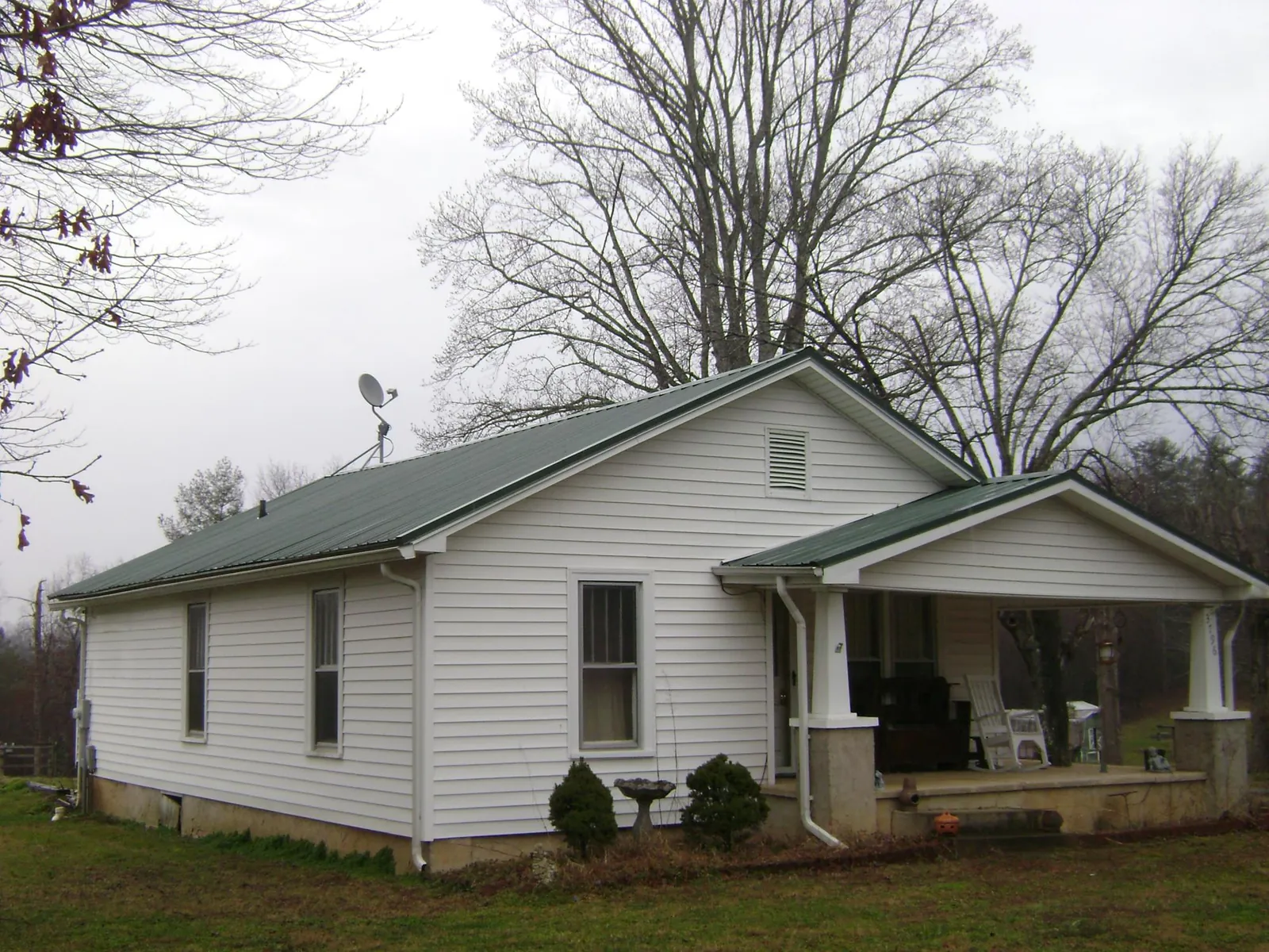Green metal roof on a white bungalow with a side porch in Rock Island