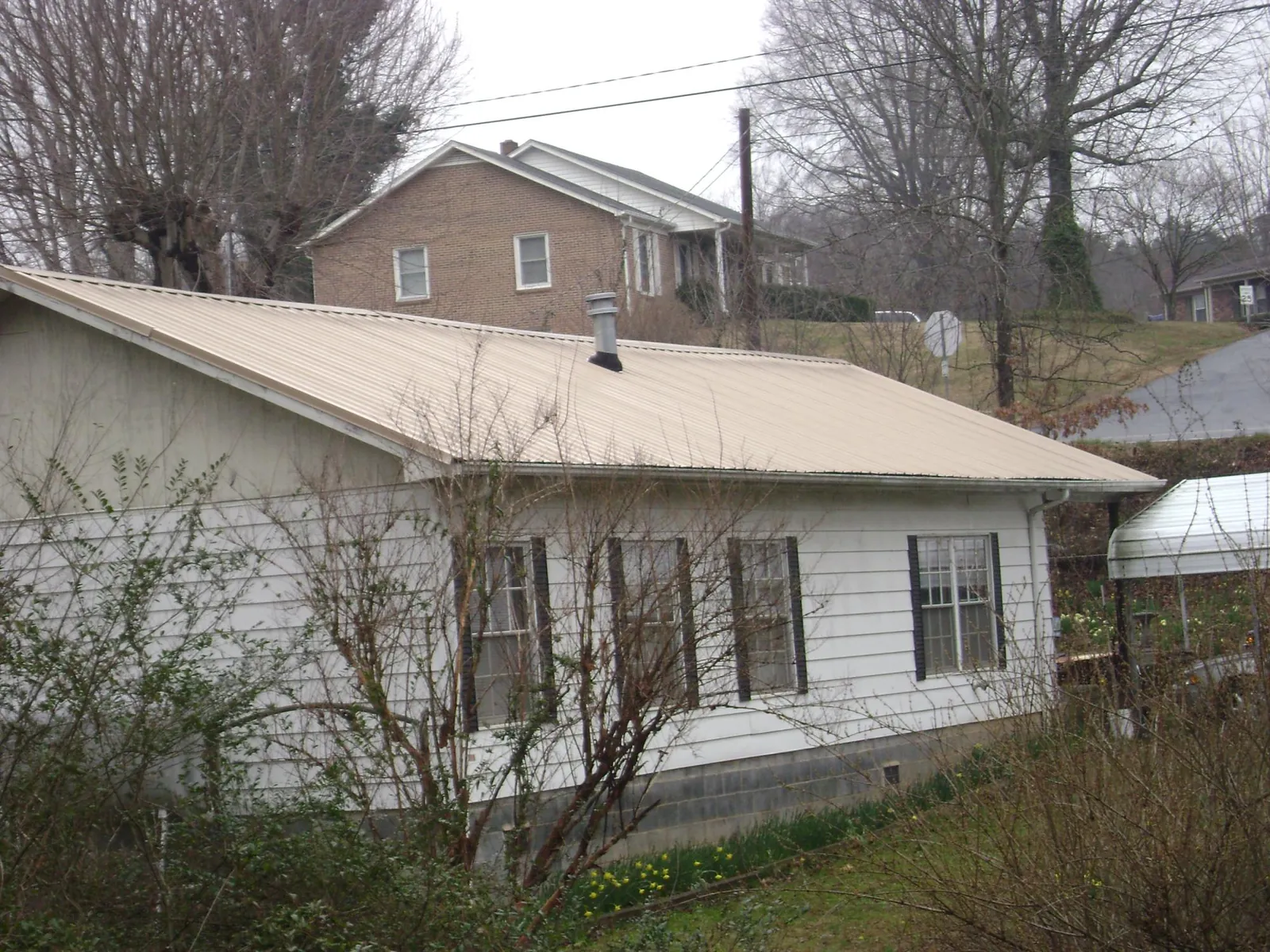Tan metal roof on a white sided house set into a hillside — Commercial Roofing by Roofing Brothers in Rock Island